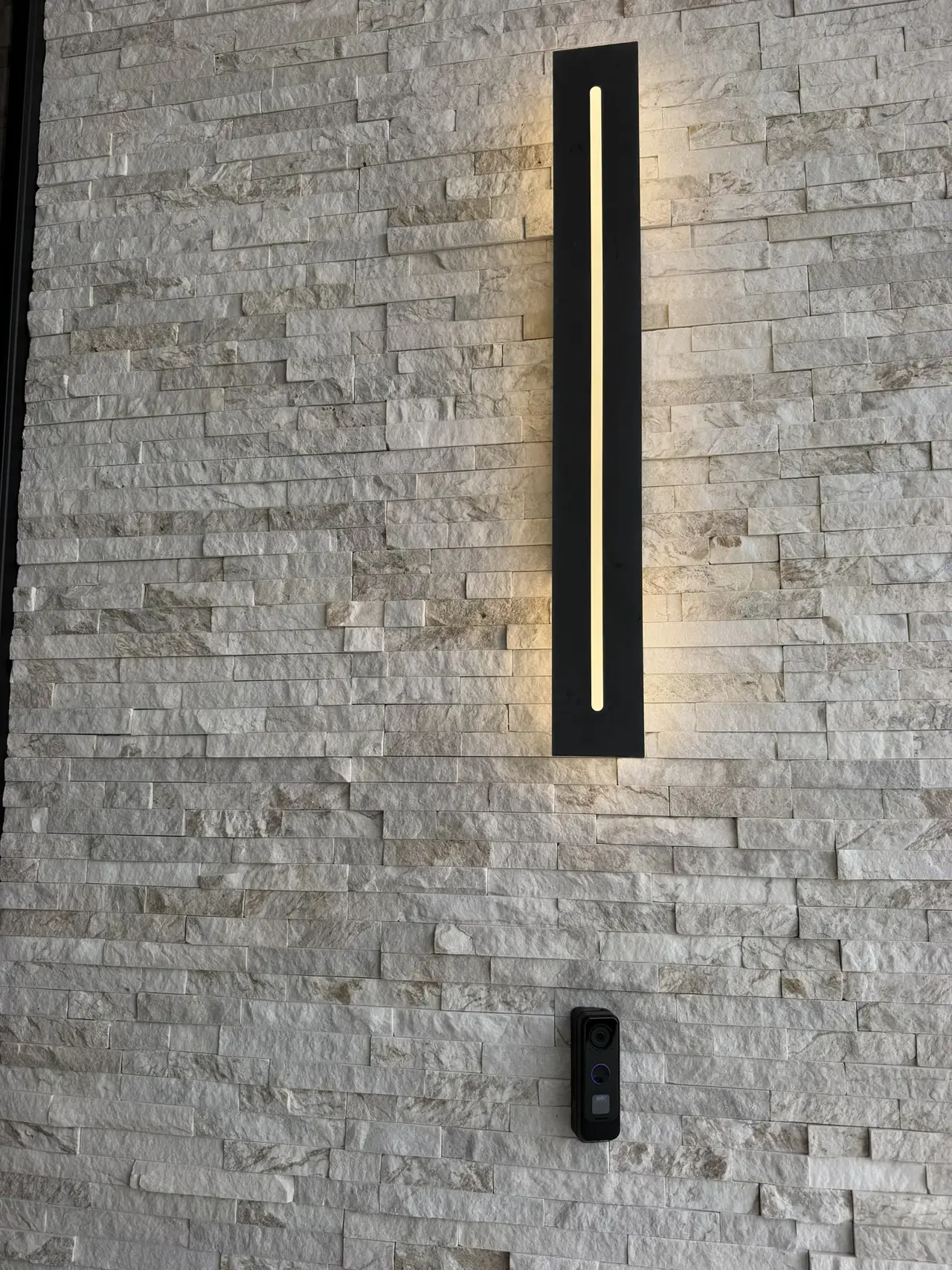 Linear LED sconce on stacked stone at a custom entry